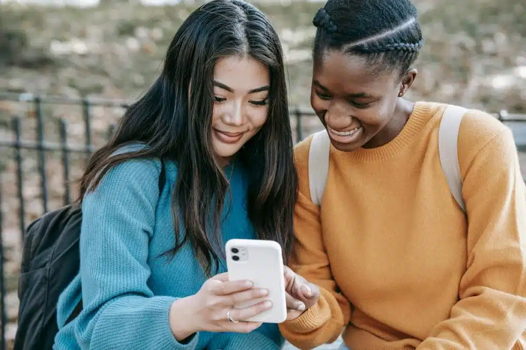 Cheerful multiethnic women browsing smartphone in park